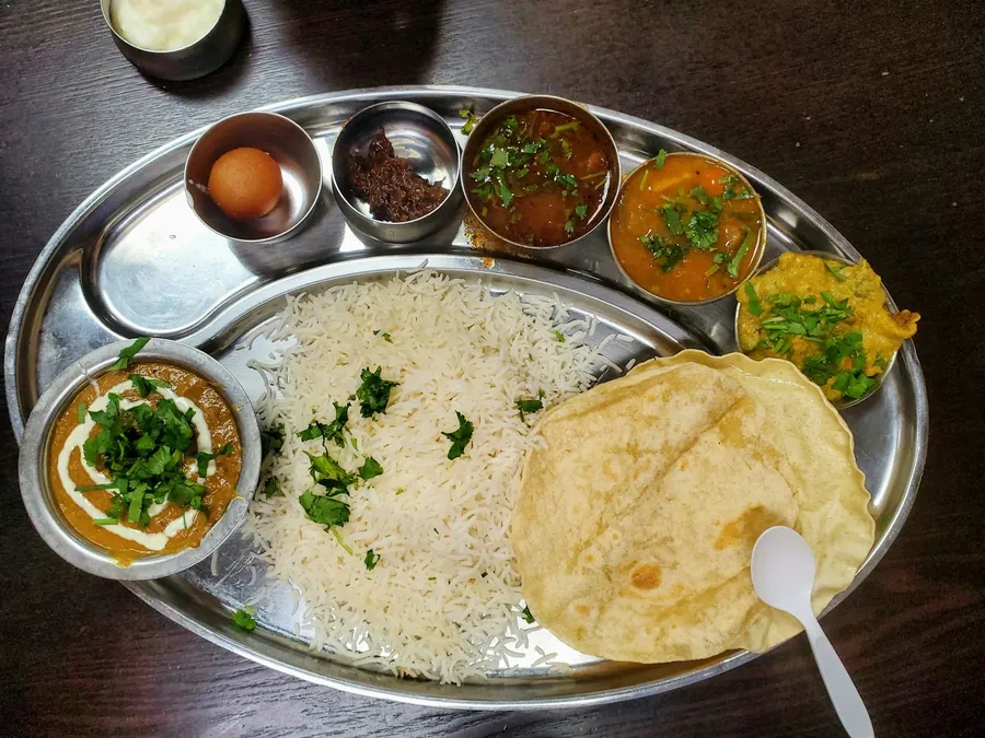 Oval silver thali with rice, naan and curries